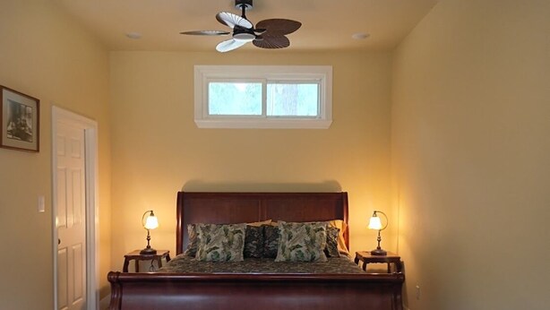 A bedroom with a large bed, two bedside lamps, a ceiling fan, and a window. - Private Woodland Cottage—Secluded Yet 5 Minutes from Town (Poplarville)