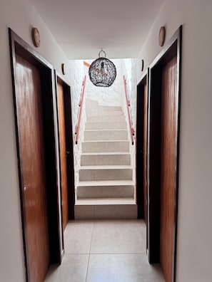 A staircase with wooden doors on either side, leading to a landing with a hanging light fixture. - Pousada Vila Mar Japaratinga (Japaratinga)