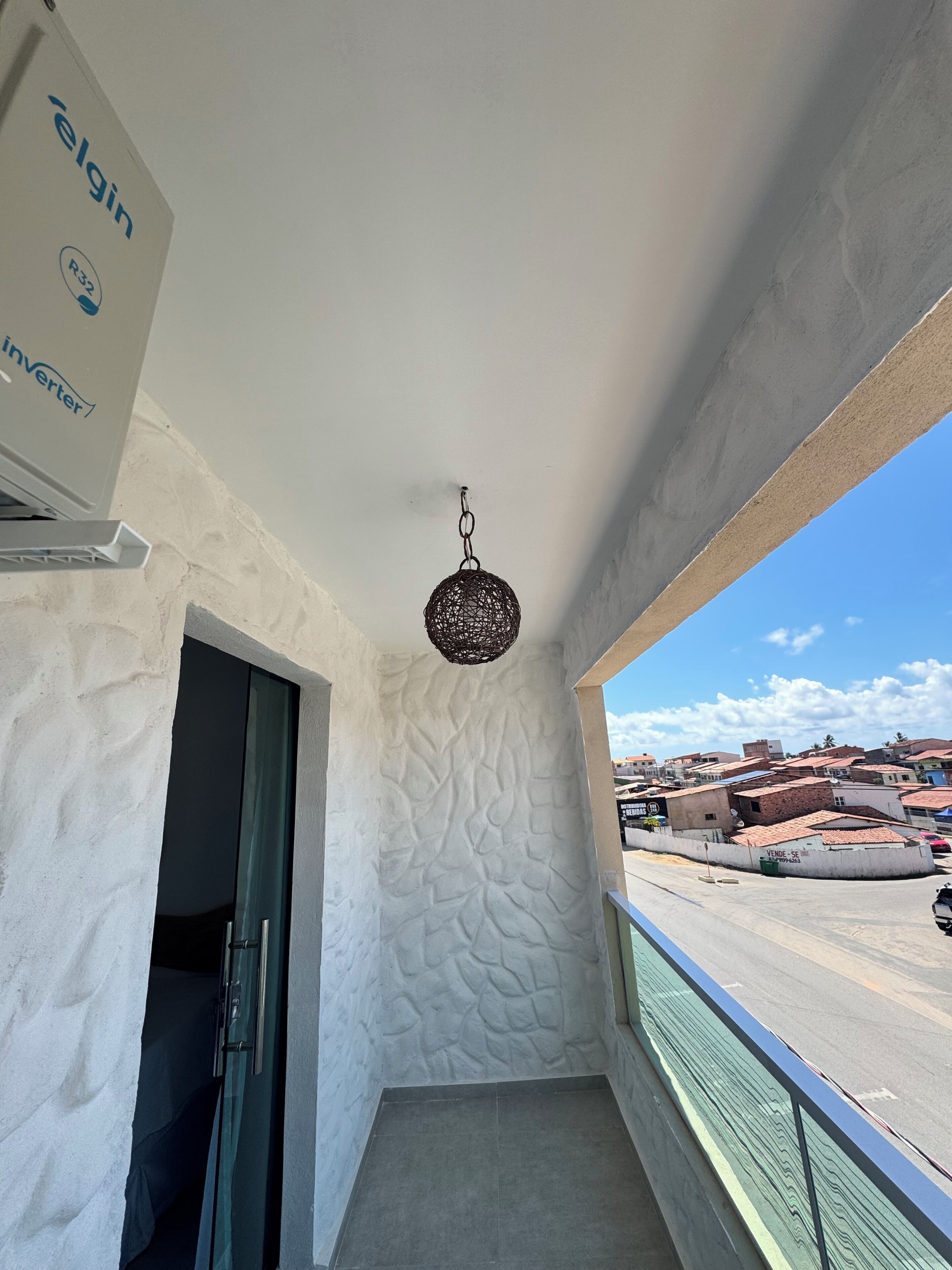 Varanda com parede texturizada, luminária pendente e vista para área residencial.