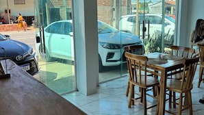 Ein geräumiges Zimmer mit einem großen Glasfenster zum Außenbereich, einem Holztisch mit Stühlen und Blick auf parkende Autos und Gebäude.