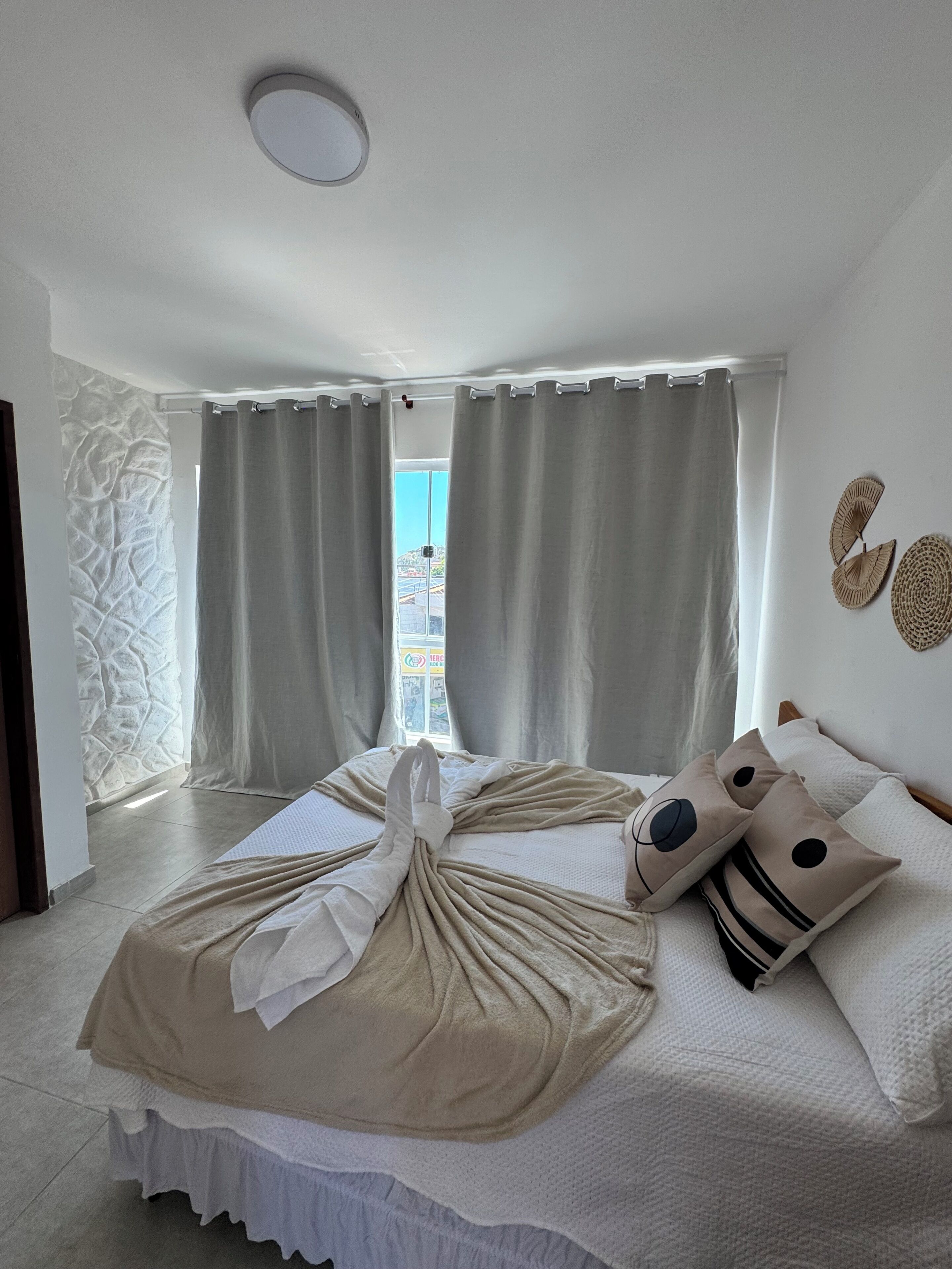 A bedroom with a bed, curtains, a wall-mounted fan, and a view through the window.