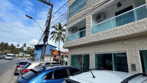 A multi-story building with a textured facade, a glass balcony on the upper floor, and parked cars in front. - Pousada Vila Mar Japaratinga (Japaratinga)