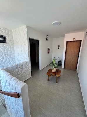 A spacious room with a stone accent wall, a wooden door, and a small table with a potted plant. - Pousada Vila Mar Japaratinga (Japaratinga)