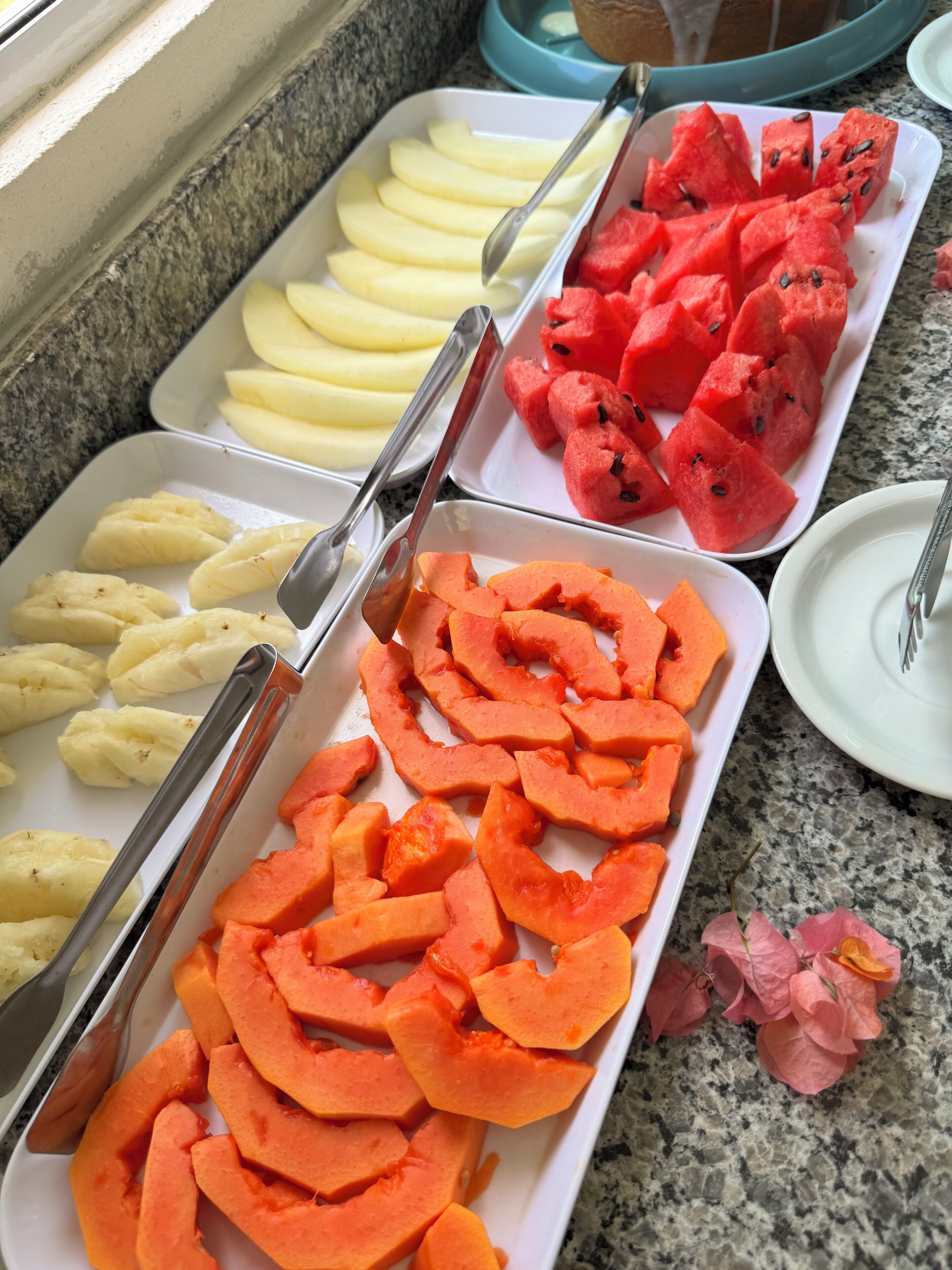 A buffet with trays of sliced fruits including apples, watermelon, and carrots.