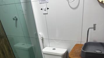 Un baño moderno con cabina de ducha de vidrio, inodoro blanco, tocador de madera con lavamanos y un cubo de basura azul.