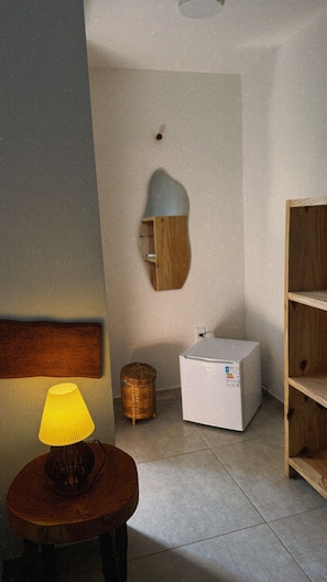 A room with a lamp, a small refrigerator, a wicker basket, and a wooden shelf unit.
