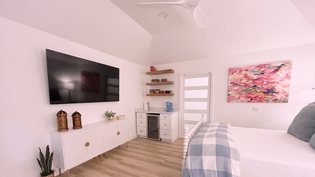 A bedroom with a bed, a desk, a television, and a painting.