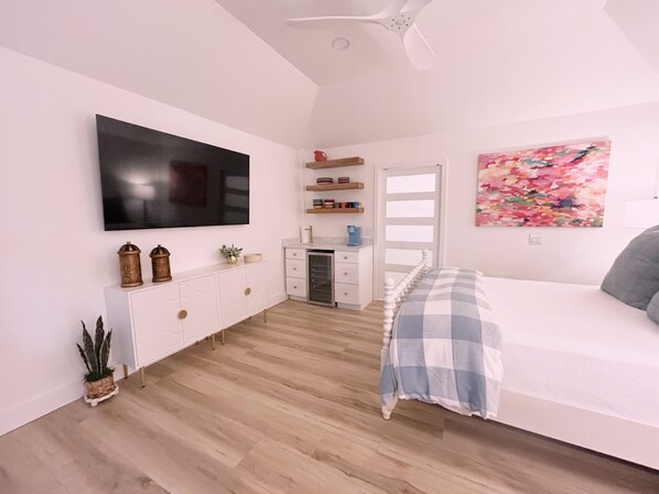 A bedroom with a bed, a desk, a television, and a painting.