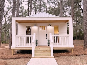 A small, white cabin with a wooden porch, two windows, and a door.