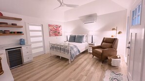 A bedroom with a bed, a chair, a bedside table, a lamp, a ceiling fan, and a window.