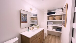 A bathroom with a white vanity, a mirror, a sink, and a shelf with folded towels.