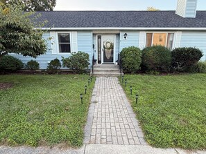 A residential house with a paved driveway leading to a front door, surrounded by well-maintained lawns and hedges.