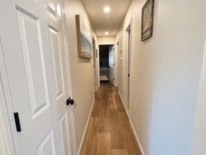 A hallway with white doors, wooden flooring, and framed artwork on the walls.