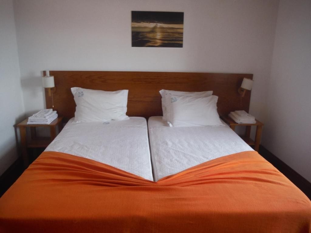 A double bed with an orange bedspread, two pillows, and a wooden headboard.