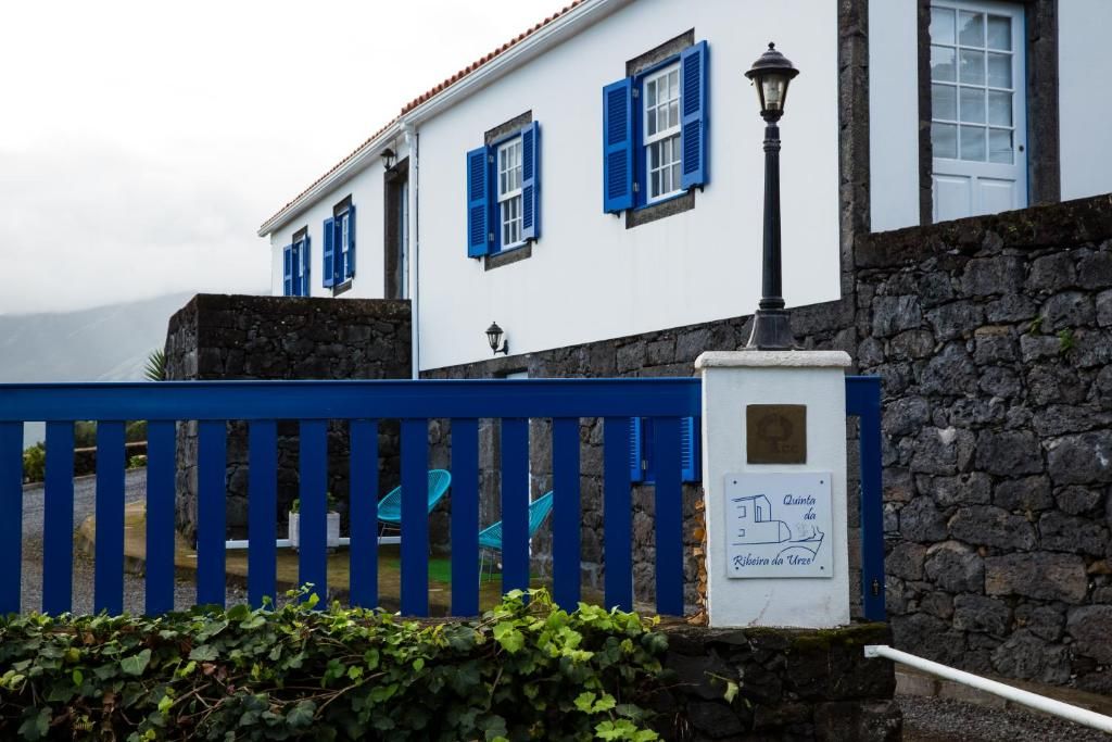 Un edificio blanco con contraventanas azules, un muro de piedra y una valla azul.