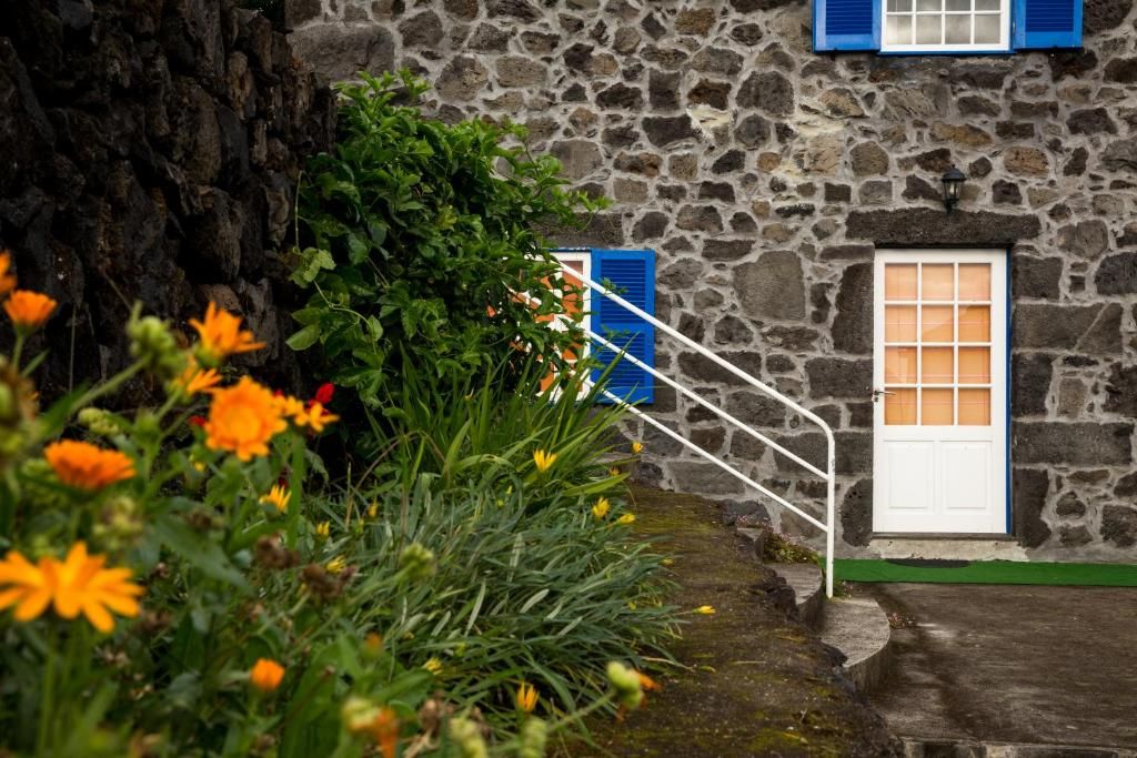Ein Steinhaus mit weißer Tür und blauen Fensterläden, umgeben von viel Grün und Blumen.