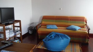 Ein Wohnzimmer mit einer Couch, einem Fernseher auf einem Schrank, einem Sitzsack und einer Wandleuchte.