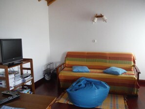 A living room with a sofa, a television on a stand, a bean bag, and a wall-mounted light fixture. - Quinta da Ribeira da Urze (Prainha de Cima Azores)