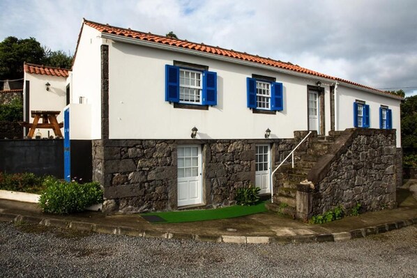 A two-story building with a stone facade, white walls, and blue shutters.