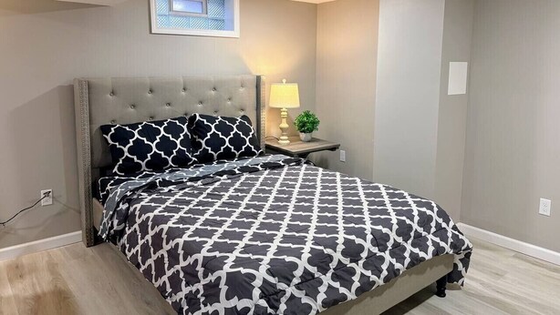 A bedroom with a bed, a nightstand, a lamp, and a window.