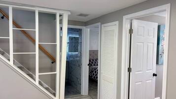 A hallway with a staircase, a door leading to a bedroom, and a bathroom with a glass shower.
