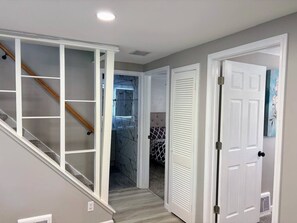 Un pasillo con una escalera, una puerta que da a un dormitorio y un baño con cabina de ducha de vidrio.