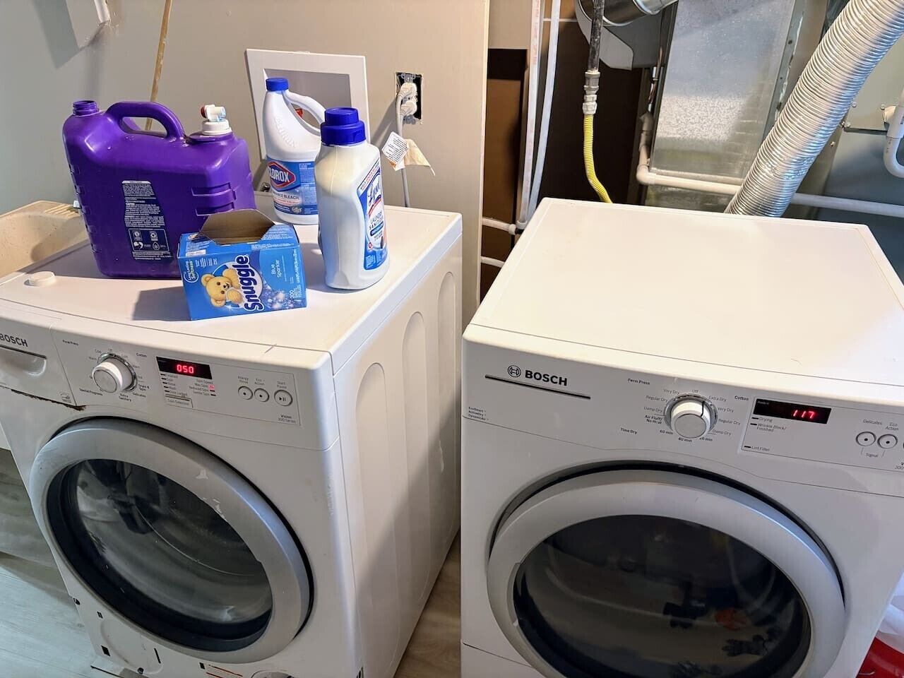 Zwei weiße Bosch Waschmaschinen mit Waschmittelbehältern und einer Waschmittelkartusche obenauf.