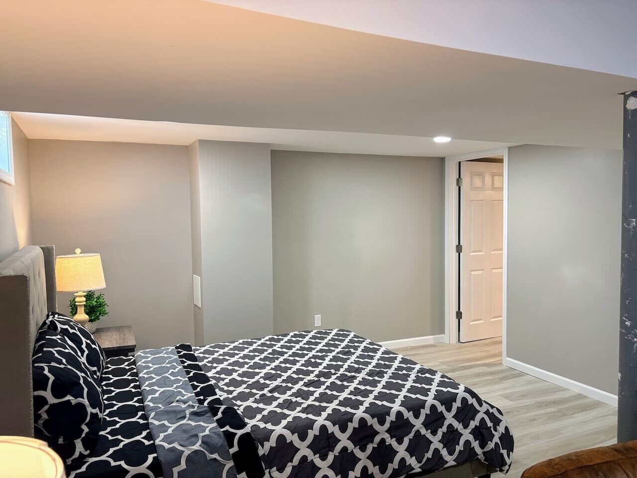 Ein Schlafzimmer mit einem Bett, einem Nachttisch, einer Lampe und einer Tür zu einem anderen Raum.