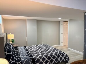 Una camera da letto con un letto, un comodino, una lampada e una porta che dà su un'altra stanza.