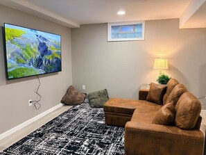Un soggiorno con una TV a schermo piatto montata a parete, un divano in pelle marrone, un tappeto decorato e una piccola finestra con cornice bianca.