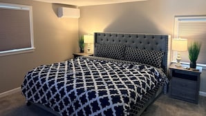 Ein Schlafzimmer mit einer gebügelten Kopfteile, einer gemusterten Tagesdecke, Nachttischen mit Lampen und einer Deckenleuchte.