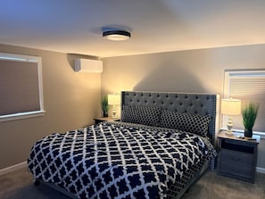 A bedroom with a tufted headboard, a patterned bedspread, bedside tables with lamps, and a ceiling light fixture. - Sweet home, King bed, fenced backyard, and parking (Buffalo)