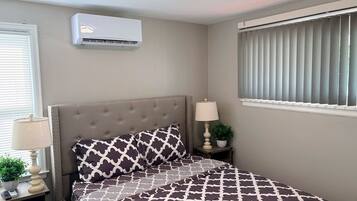 A bedroom with a bed, a nightstand, a lamp, a potted plant, and an air conditioning unit.