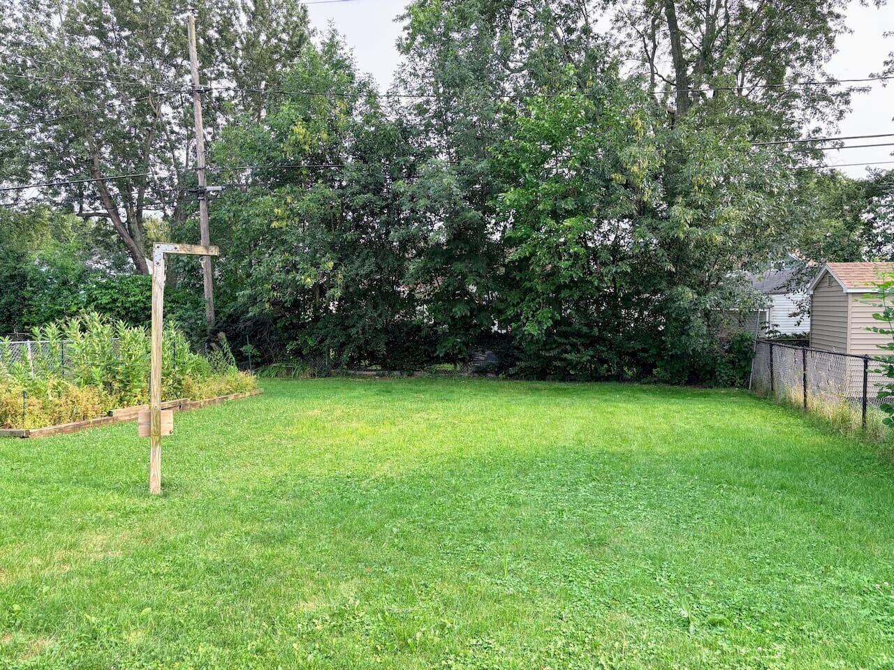 Ein Garten mit Gras, einem hölzernen Bauwerk, Bäumen und einem Zaun.
