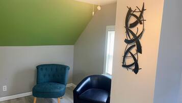 A room with a sloped ceiling, a green wall, two chairs, and a wall-mounted abstract art piece.