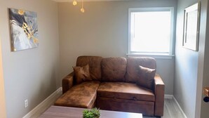 A living room with a brown leather sectional sofa, a coffee table with a plant, a ceiling fan, and a window with blinds.