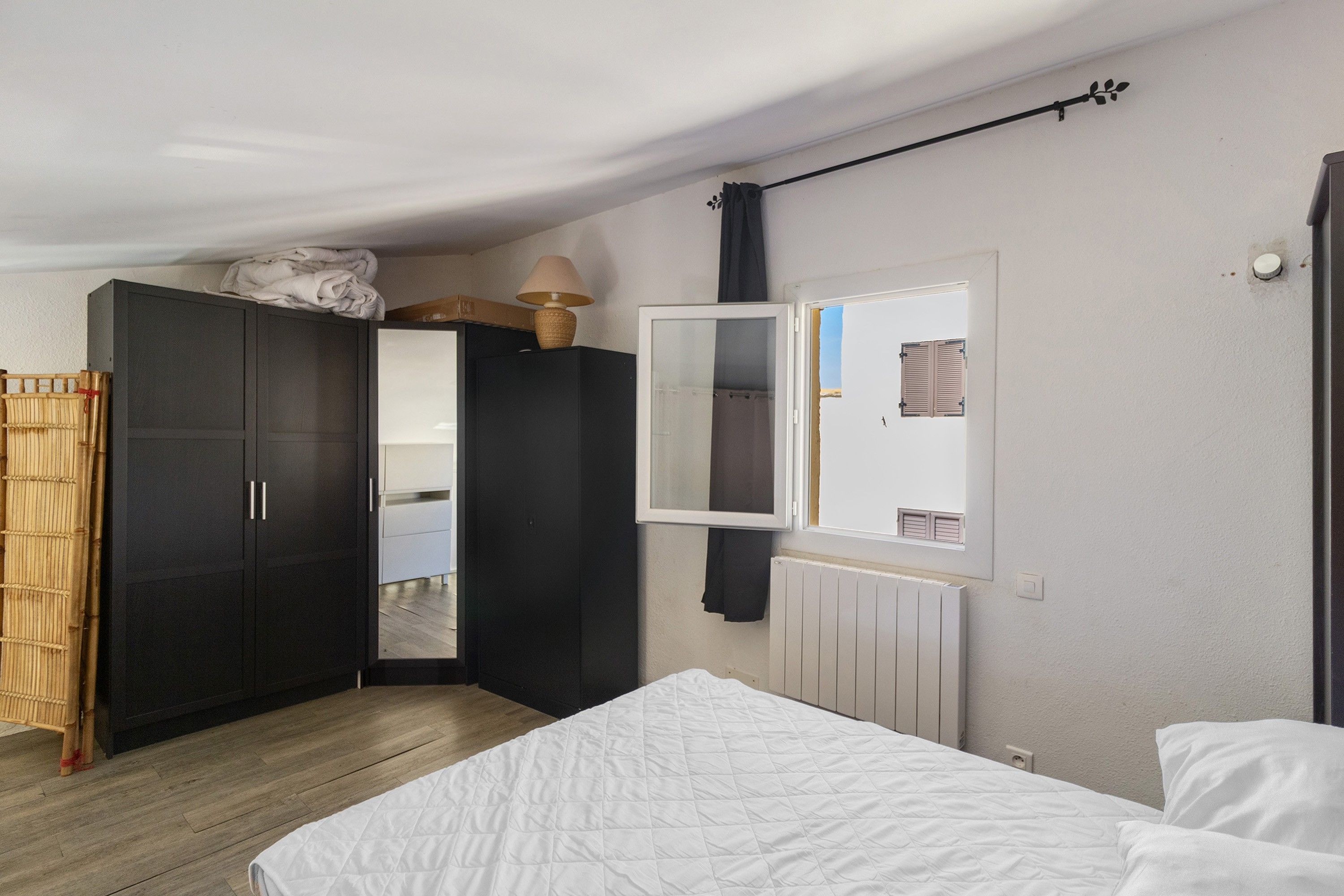 Een slaapkamer met een bed, een kledingkast, een spiegel en een radiator.
