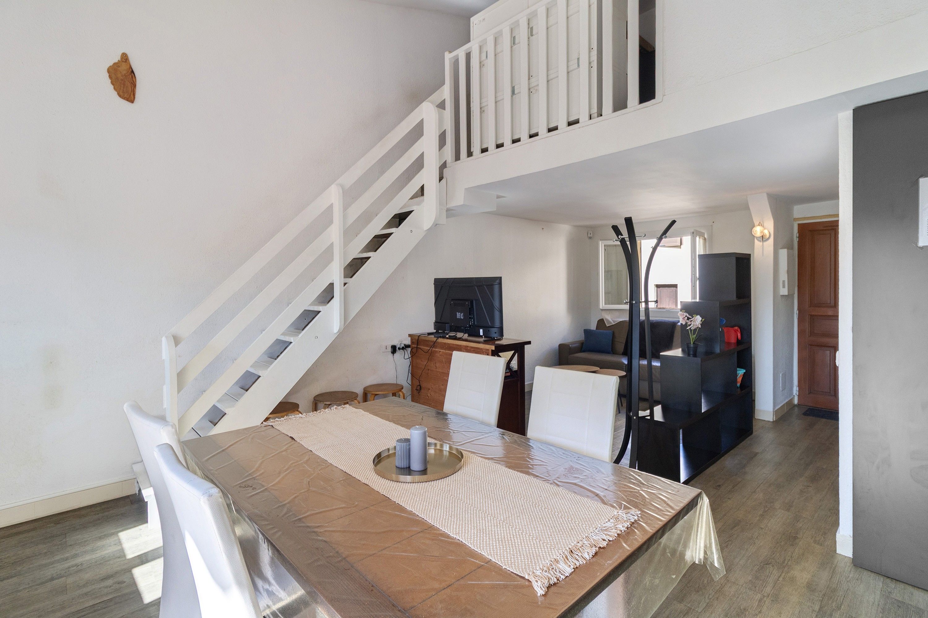 A dining area with a table, chairs, a TV, and a staircase.