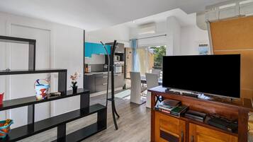 Een moderne woonkamer met een flatscreen televisie, een houten tv-meubel en een keuken in de achtergrond.