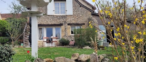 A stone house with a bell tower, a garden with rocks and plants, and a clear sky.