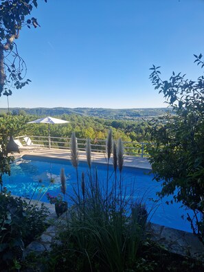 A swimming pool with a view of a distant building and surrounding greenery. - Vacation rental, house, in the heart of the Périgord Noir: "Le Lascaux" (Adults Only, 2 people) (Le Bugue)