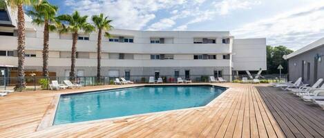 A swimming pool with lounge chairs, palm trees, and a multi-story building.