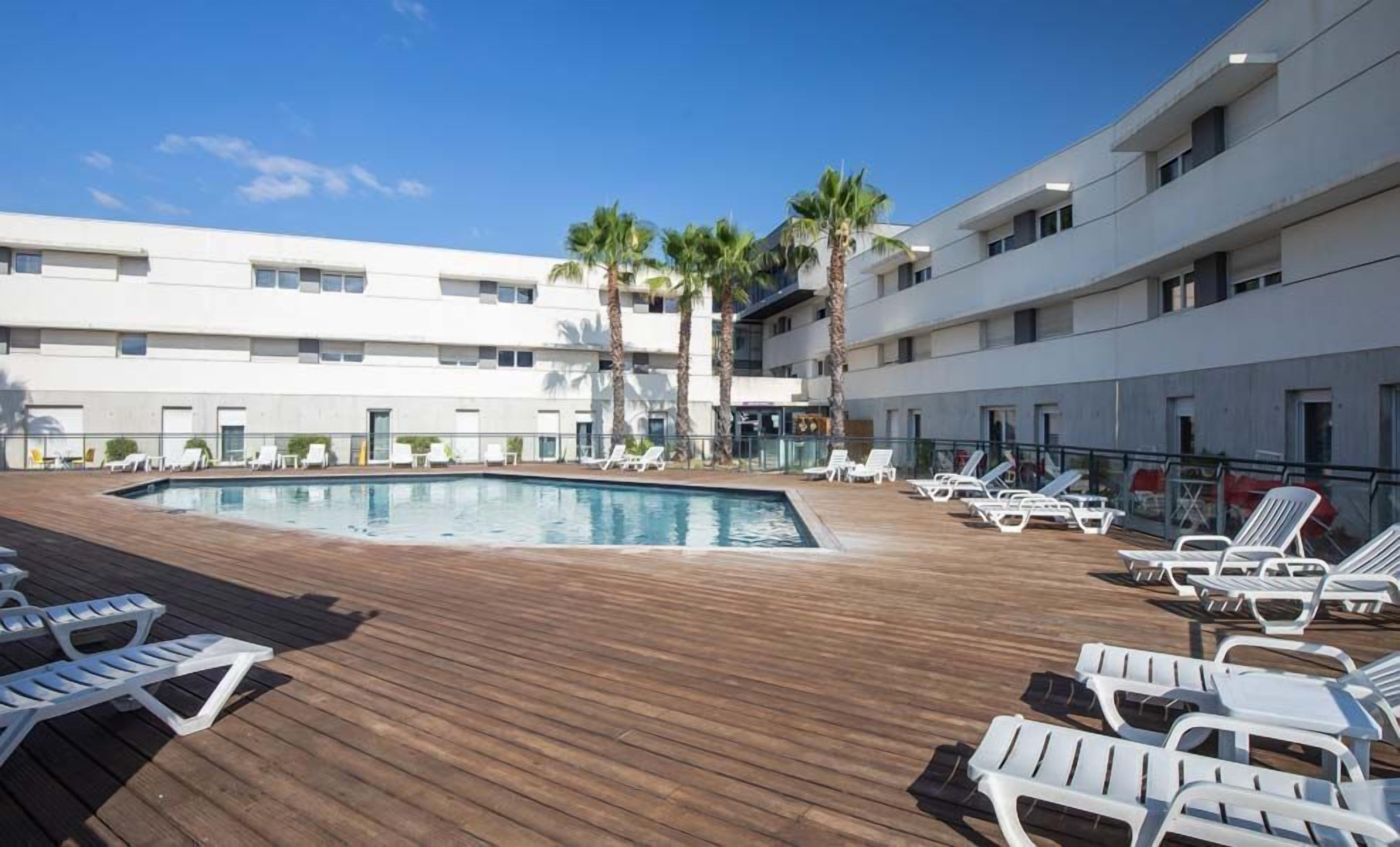 A pool area with lounge chairs and a building with multiple floors.