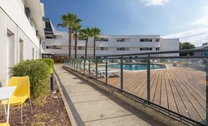 A poolside area with a wooden deck, lounge chairs, and a building with multiple floors.