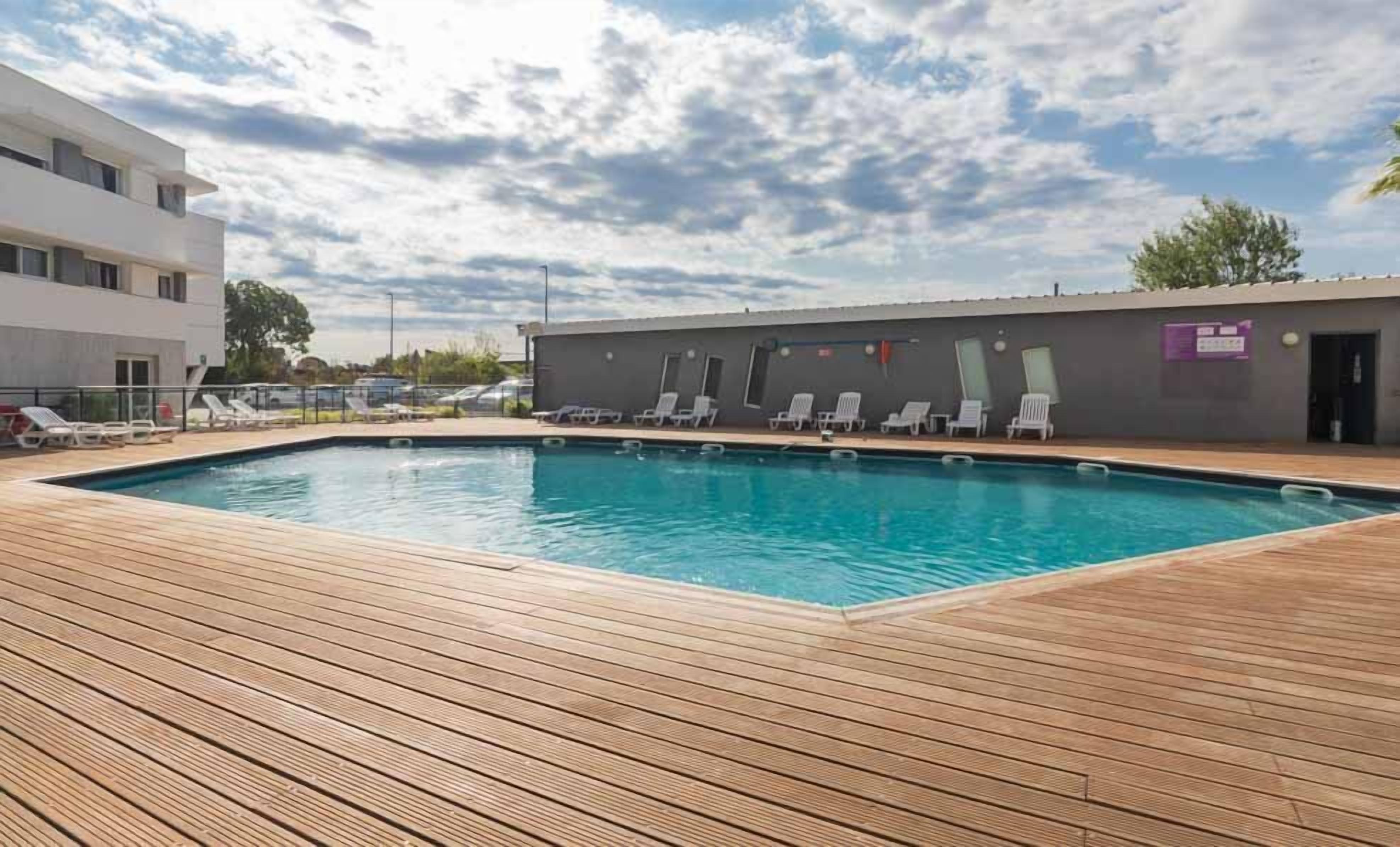 A swimming pool with a wooden deck, lounge chairs, and a building with a sign.