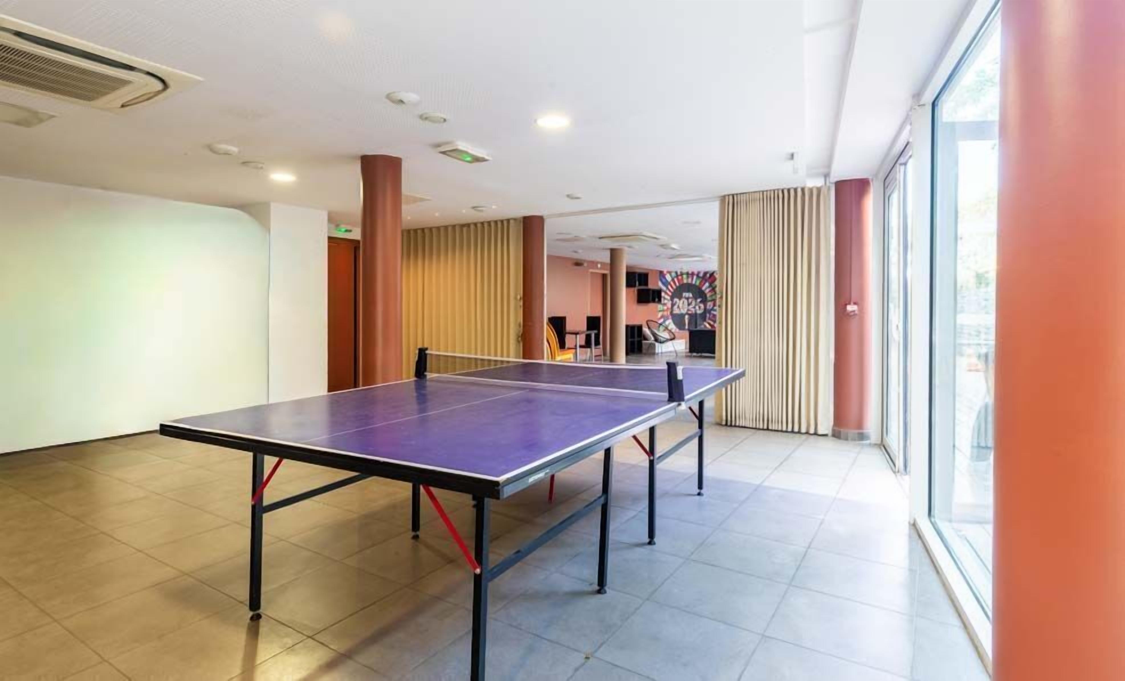 Een kamer met een tafeltennistafel, een groot raam en een deur naar een ander gedeelte.