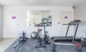 Un gimnasio con equipo de ejercicio, incluyendo una cinta de correr, bicicleta estática, elíptica y máquina de remo.