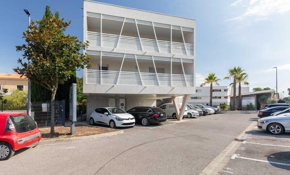 Un edificio moderno con techo plano, varios balcones y un estacionamiento con varios automóviles.