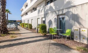 Un edificio con fachada moderna, zona de estar al aire libre con sillas y un camino que lleva a la entrada.