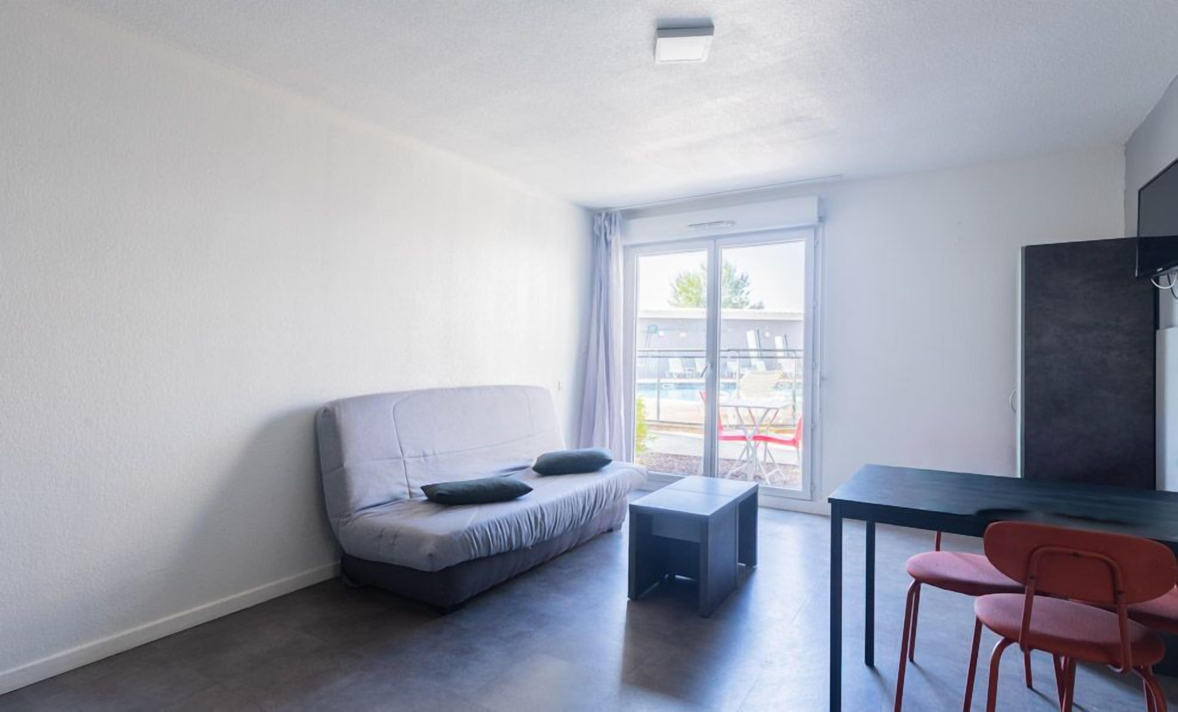 Quarto moderno com sofá cinzento, uma mesinha e cadeiras vermelhas.
